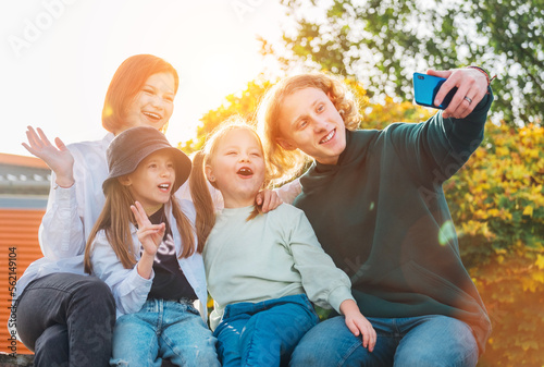 Portraits of three smiling sisters and brother teen taking selfie portrait using a modern smartphone camera. Careless happy young teenhood, childhood time and modern technology concept image.