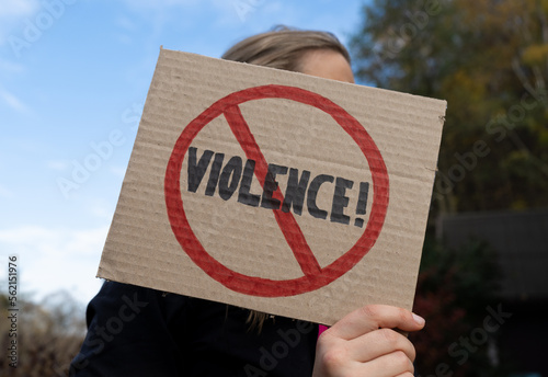 Woman holding a cardboard banner sign with word Violence strikethrough. Female protester with Stop Violence placard at protest rally demonstration. © Longfin Media