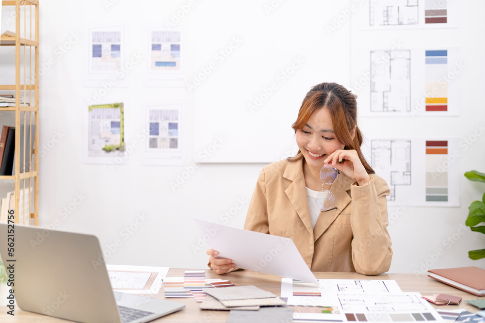 Young asian female interior designer or architect working on creative project with drawing, material sample & laptop computer in office. Business of Real estate, home decoration & renovation concept. Young asian female interior designer or architect working on creative project with drawing, material sample & laptop computer in office. Business of Real estate, home decoration & renovation concept.