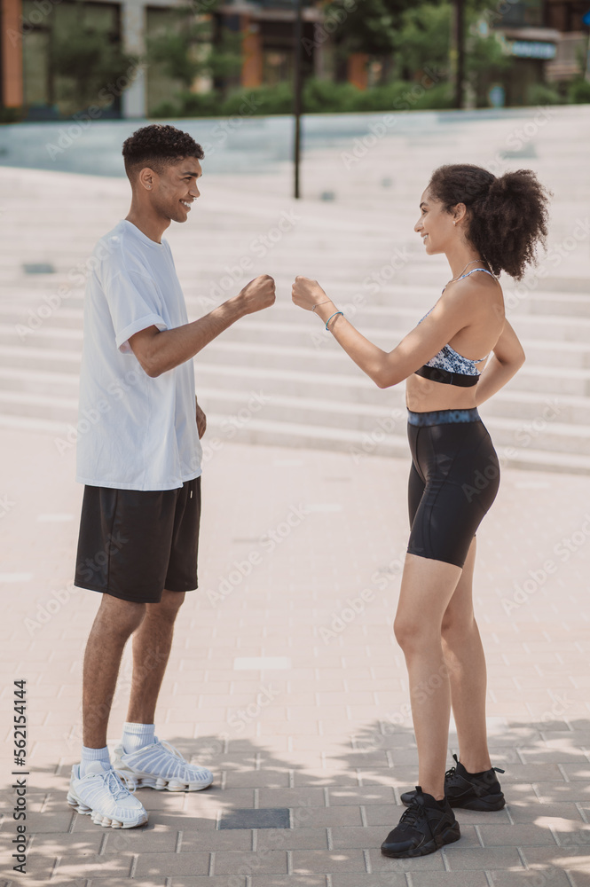 Fototapeta premium Two cheerful athletes fist-bumping one another outdoors