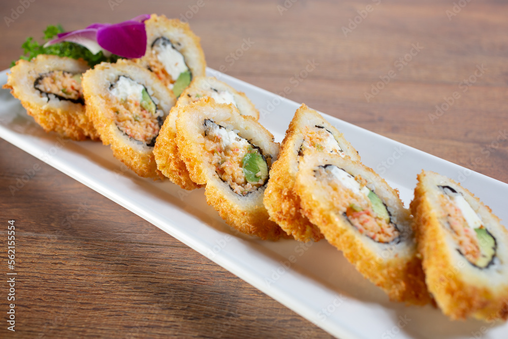 A view of a sushi roll featuring spicy crabmeat, cream cheese, avocado, and a deep fried crust.