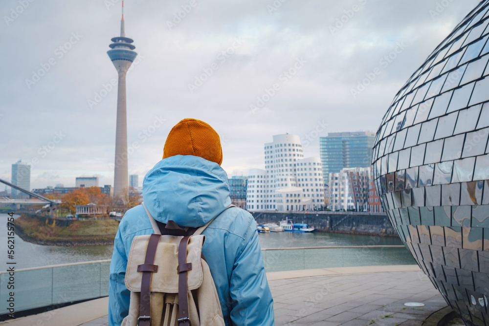 autumn or winter travel to Dusseldorf, Germany. young Asian tourist or student in blue jacket and yellow hat ( symbol of Ukraine) walks through sights of European city. beautiful view in the Media Bay