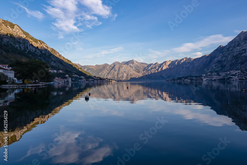 Panoramic view of bay of Kotor at sunrise in summer, Adriatic Mediterranean Sea, Montenegro, Balkans, Europe. Fjord winding along coastal towns. First sunbeams on Lovcen mountains. Water reflection