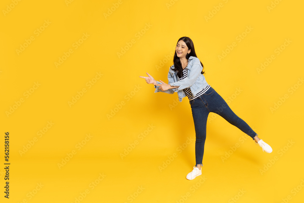 Young beautiful Asian woman standing and pointing to empty copy space isolated on yellow background, Full body composition Young beautiful Asian woman standing and pointing to empty copy space isolated on yellow background, Full body composition