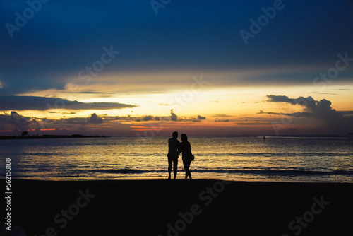 Young couple looking far away at the seaside in summer evening. Man's and woman's silhouettes on the beach.