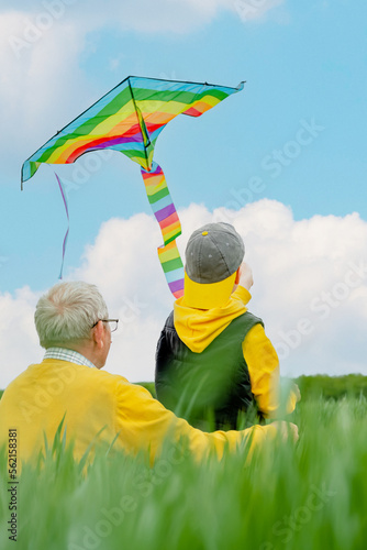 Focus on the rainbow kite flying, an elderly man and a grandson are looking at the sky, turned back. Family active outdoors game and playtime positive
