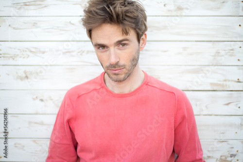 Portrait of handsome guy standing in front of a wooden background. He wears a red sweater.