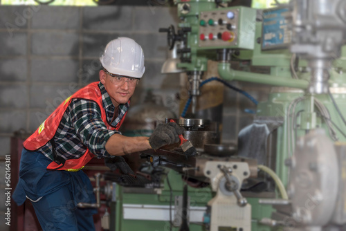 Engineer working on a metal lathe machine in a factory background that is blurry
