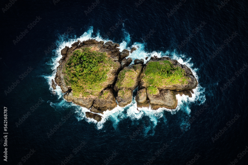 View from above, stunning aerial view of a little rocky island bathed by a rough sea at sunset. Lombok Island, West Nusa Tenggara, Indonesia.