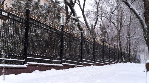 Large metallic fence and snow covered road in cold winter day city landscape