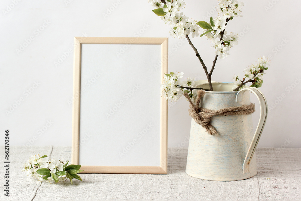 Fototapeta premium spring mockup with an empty frame on the table and flowering branches in a jug.