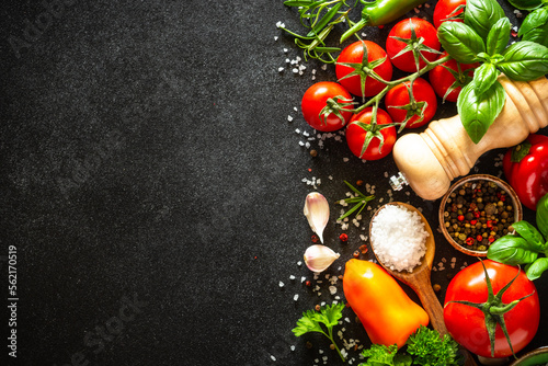 Food background on black stone table with fresh vegetables, herbs and spices. Ingredients for cooking with copy space.