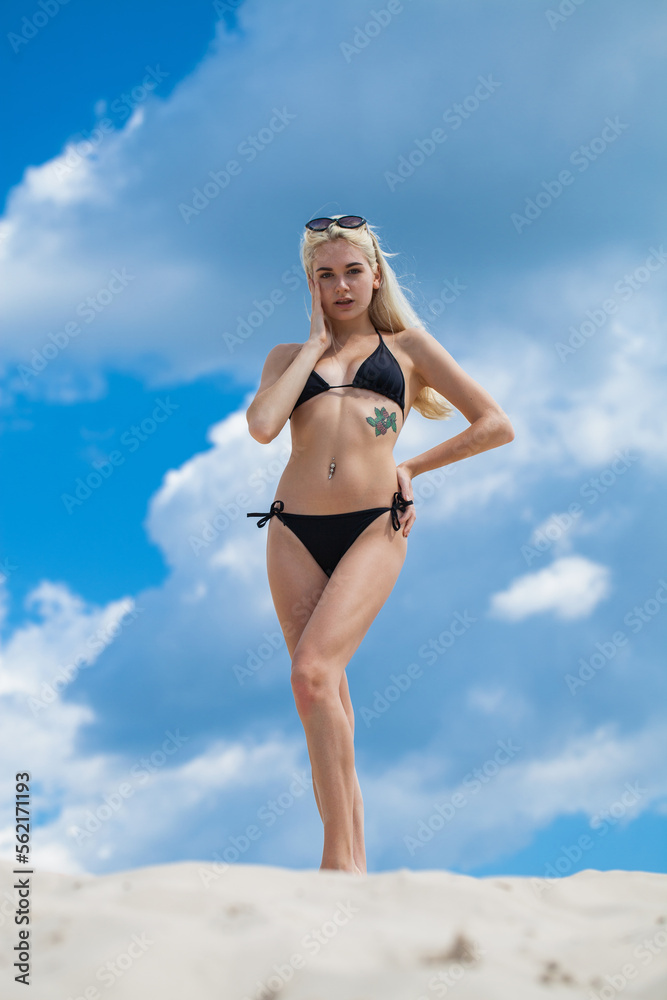 Young beautiful woman in black bikini posing on a sand pit background