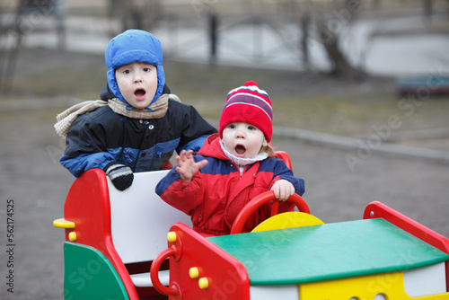 Two small children play with a car on the playground during the cold season.