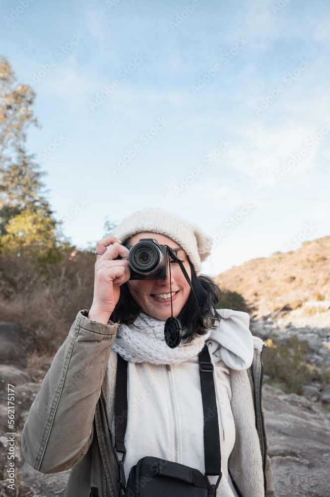 vertical portrait of young woman on the mountain taking a photo of the landscape