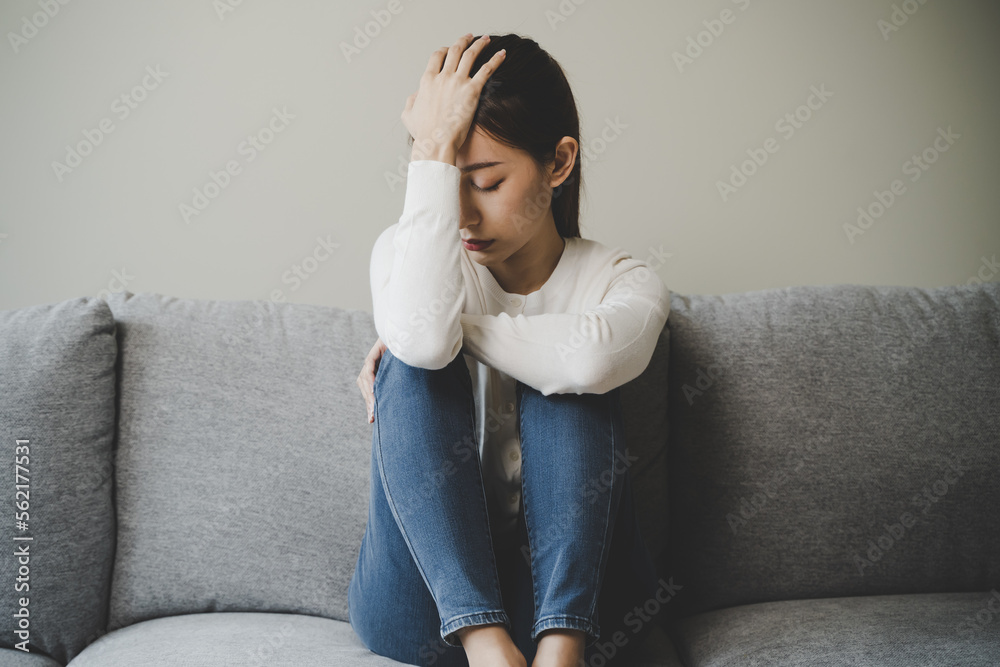 Unhappy anxiety young Asian woman covering her face with pillow on the cough in the living room at home. - obrazy, fototapety, plakaty 