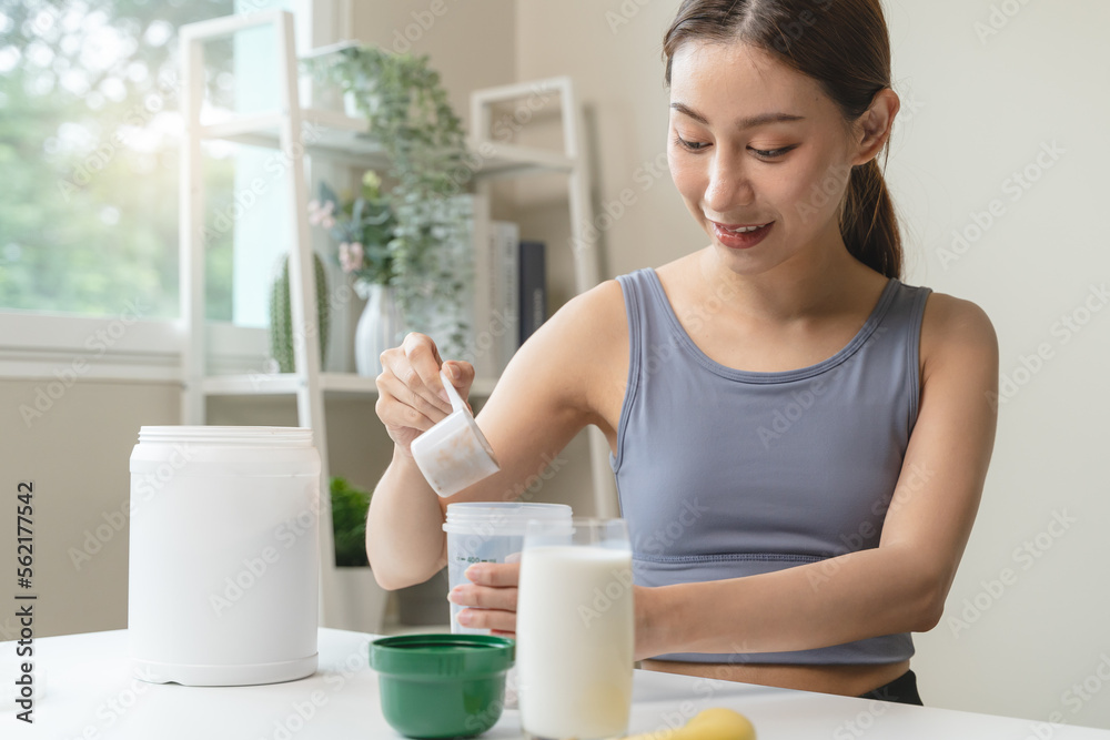 Young sporty woman pouring protein powder into a cup to make replacement food meal after workout Young sporty woman pouring protein powder into a cup to make replacement food meal after workout