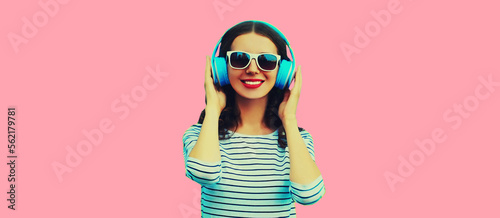 Portrait of happy smiling young woman with headphones listening to music on pink background