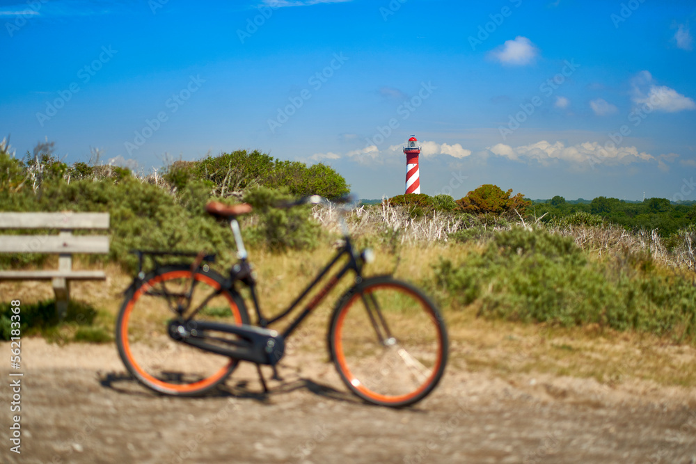 Lighthouse on the horizon in the colors red and white. Ladies bike out of focus. Dutch landscape on a beautiful summer day. Holland, Zeeland, Haamstede.