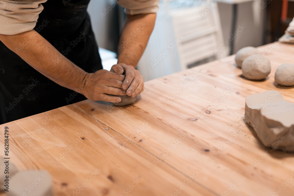 Kneading piece of raw grey clay by man hands on wooden table. DIY potter hobby Kneading piece of raw grey clay by man hands on wooden table. DIY potter hobby