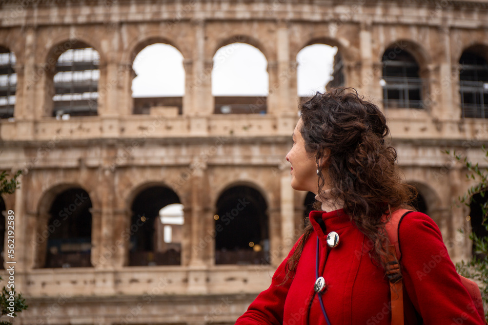 Woman in red coat looking from outside the Roman Colosseum, in Rome, in Italy
