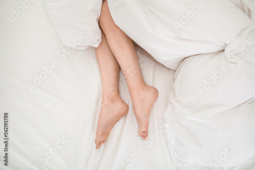 Lying on bed female legs under blanket, cropped shot