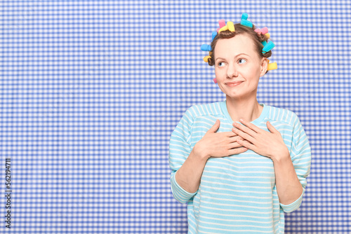 Happy dreamy cute young woman with colorful hair curlers on head