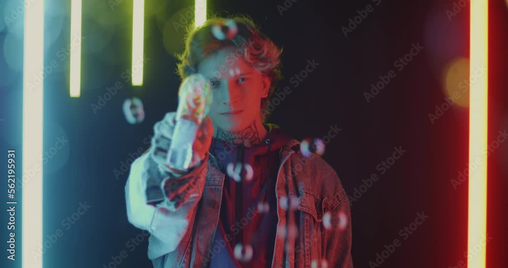 Portrait of playful young man holding toy gun and having fun with soap bubbles at night against neon background. Adults and joy concept. Portrait of playful young man holding toy gun and having fun with soap bubbles at night against neon background. Adults and joy concept.