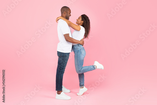 Side view of loving african american couple hugging and looking at each other on pink studio background, copy space