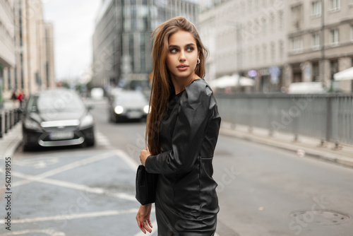Beautiful urban woman model in a fashion black leather dress on the background of a modern city