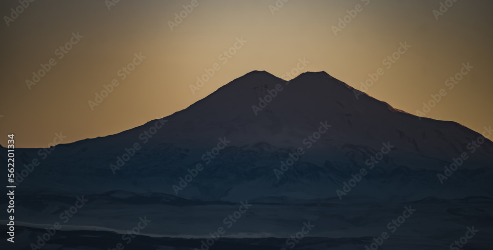 Panorama of the mountain range of the Caucasus Mountains and Elbrus at sunset, view of the mountain peaks in winter in the evening at sunset