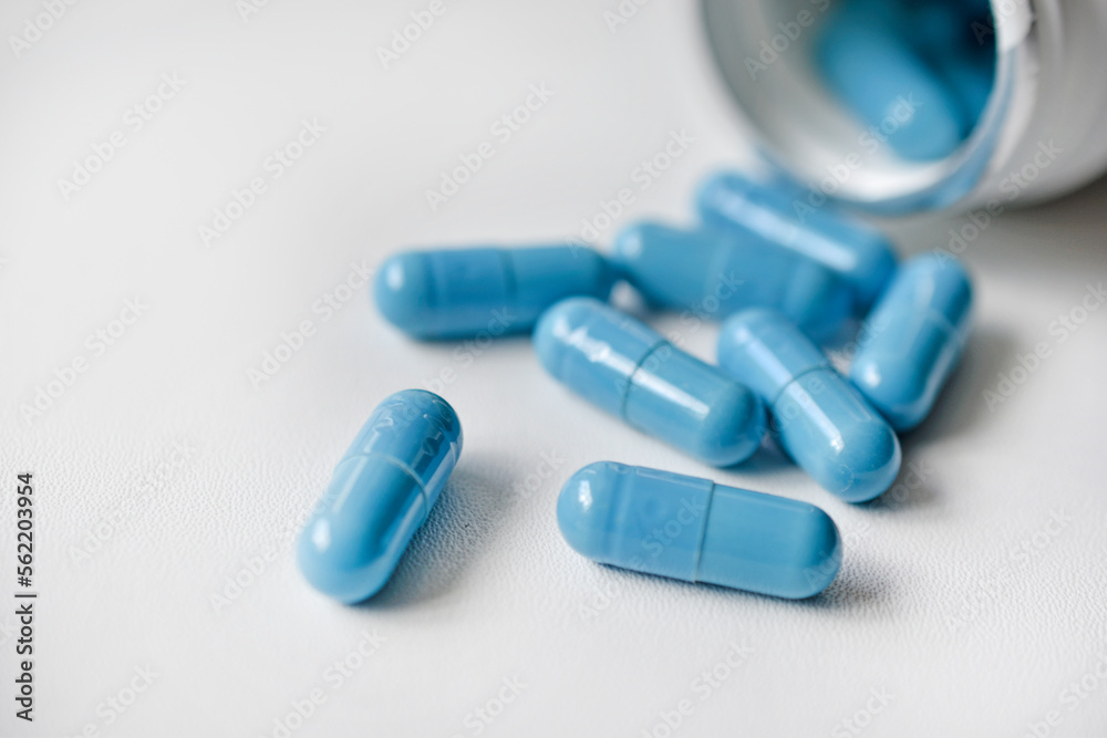 Blue capsules with medicine on a white background. The medicine poured out of the jar. Capsules. Blue capsules with medicine on a white background. The medicine poured out of the jar. Capsules.