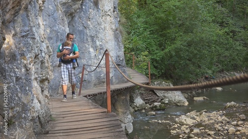 Father baby wearing passing on wooden bridge above mountain river, free parent