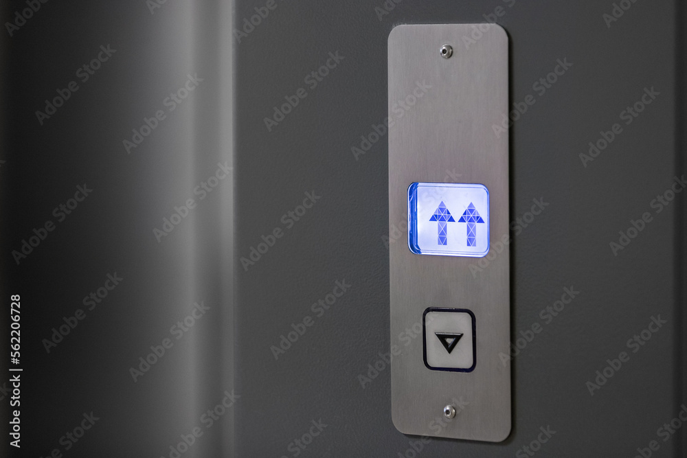 Metal panel with an elevator call button and an indicator of the direction of movement of the elevator car in blue