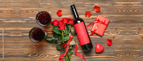 Glasses of wine, bottle, rose flowers and gift on wooden background. Valentine's Day celebration