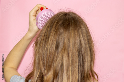 blonde hair girl woman holding ponytail up or silicone soft shampoo brush with bristles isolated on pink.hair growth stimulating scalp massage healthy long curly hair.young woman back view hands up