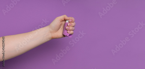 The girl's hand holds an inhaler from asma. inhaler in hand on purple background with copy space. the concept of easy breathing, atma, diseases of the upper respiratory tract photo