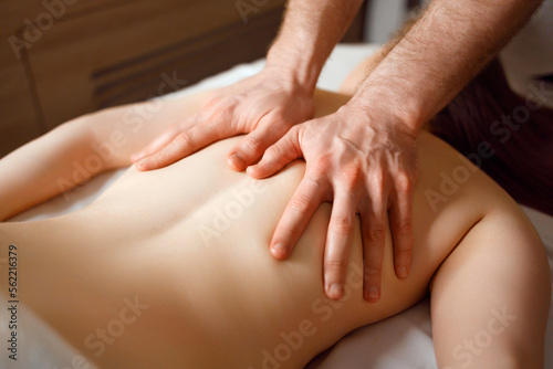 Close-up of hands of male massage therapist doing back massage to woman client of spa salon