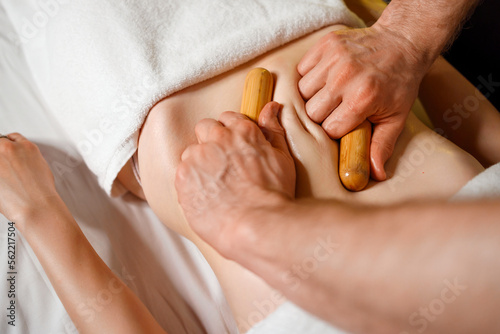 Hands of a male masseur massaging a woman's abdomen with small bamboo sticks. Enjoying spa treatments