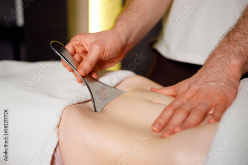 Abdominal massage of a woman with a special metal instrument, spa theraphy, close up