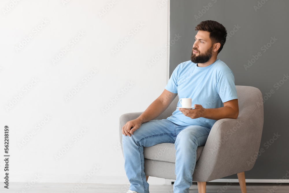 Handsome man with cup of coffee sitting in armchair near black and white wall Handsome man with cup of coffee sitting in armchair near black and white wall