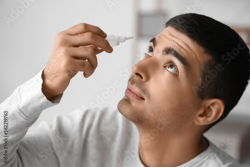 Young man using eye drops a...