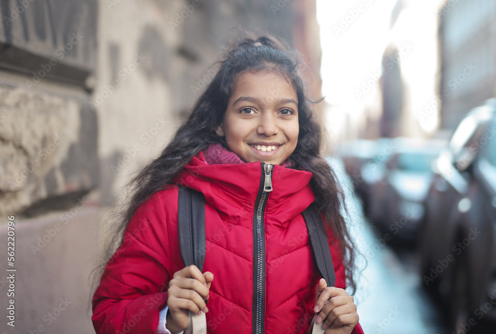 Fototapeta premium portrait of little girl with backpack on her shoulder on the street
