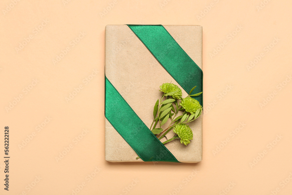 Gift box tied with green ribbon and chrysanthemums on color background