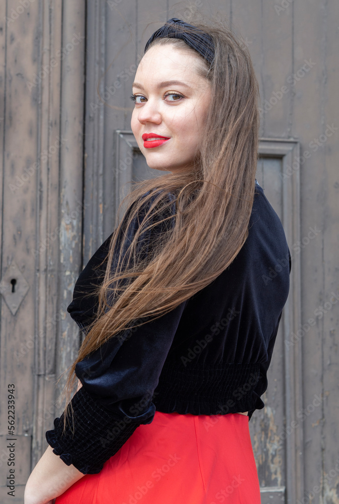 Fototapeta premium Mujer joven, blanca, caucásica mirando de frente sonriendo, con labios rojos y cabello castaño muy largo en el exterior.