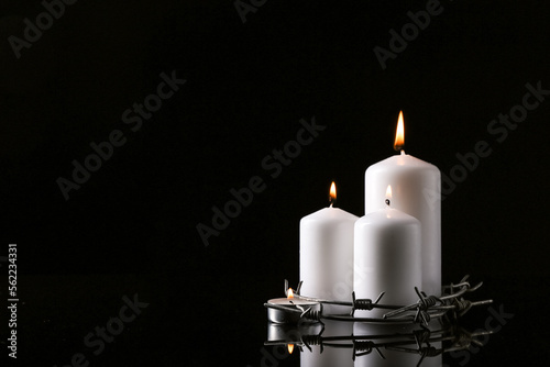 Burning candles and barbed wire on dark background with space for text. International Holocaust Remembrance Day photo