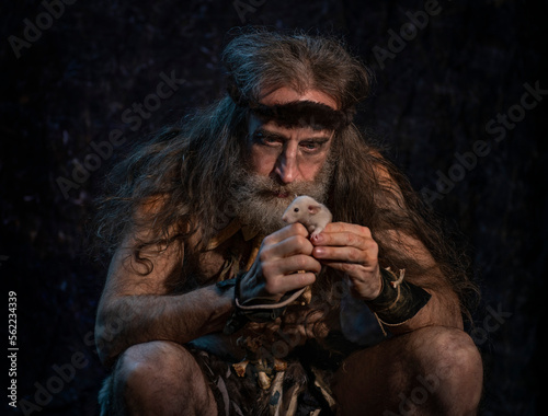 A bearded man with long gray hair holds a rat in his hands and looks at it