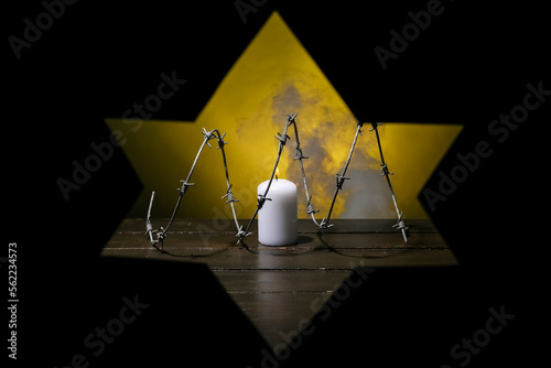 Burning candle and barbed wire on table visible through shape of David star on black background. International Holocaust Remembrance Day