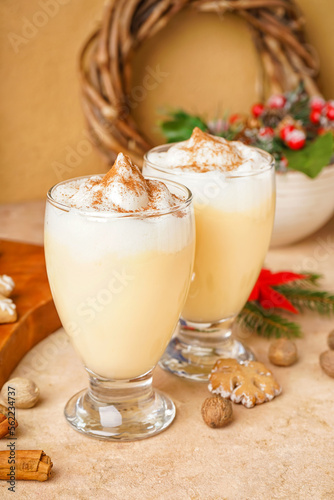 Glasses of tasty eggnog cocktail and Christmas decor on color background