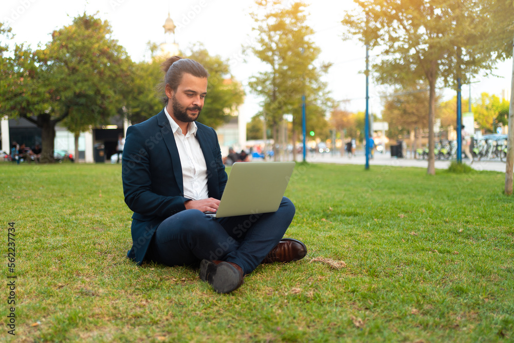 Handsome hispanic male businessman sitting lotus position in public park use laptop Handsome hispanic male businessman sitting lotus position in public park use laptop